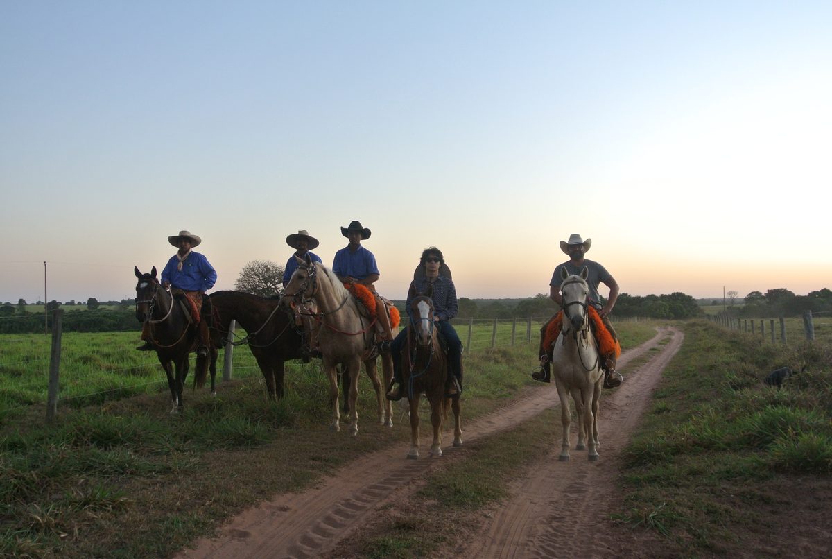 Riders on horseback on a dirt road at dusk.