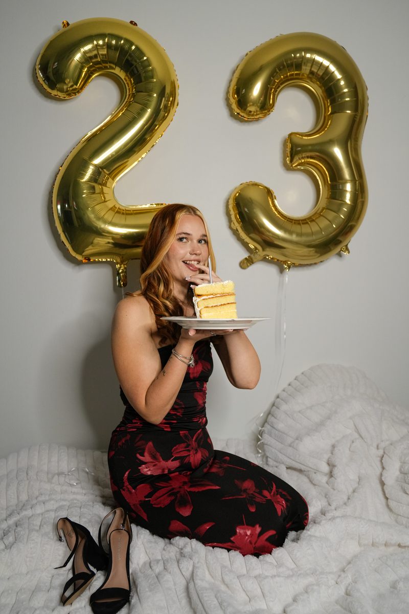Birthday portrait with gold 23 balloons, holding a slice of cake.